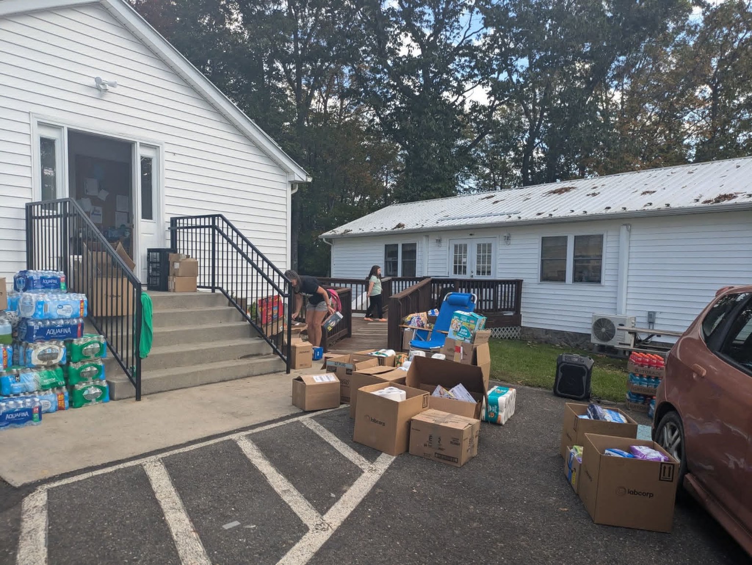 OBOG relief supplies staged outside a white building while people organize and distribute water and boxes.
